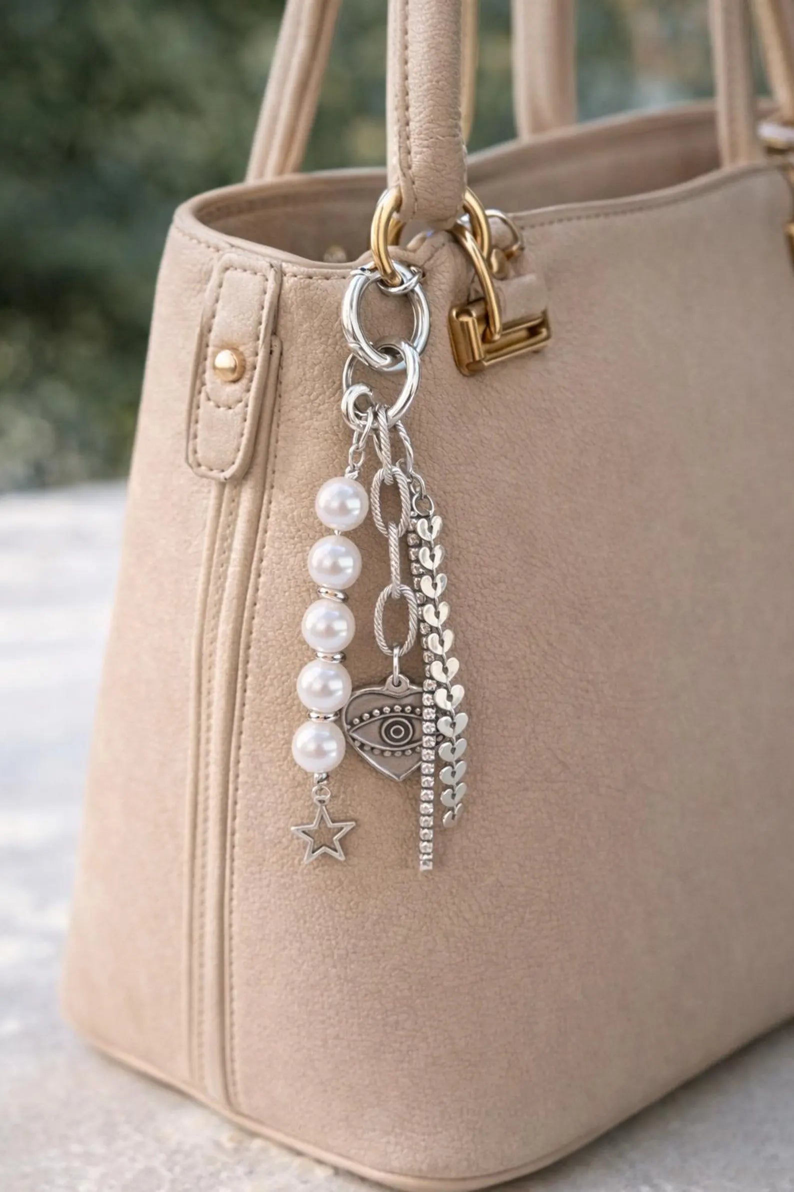Beige handbag with a keychain featuring pearls and charms on a blurred background