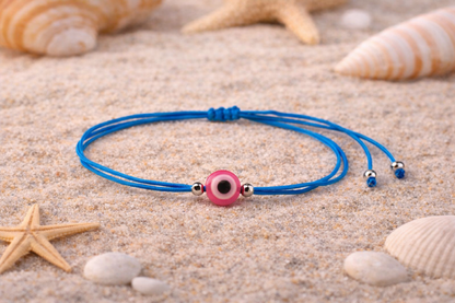 Blue bracelet with a pink evil eye charm on sand with starfish and shells