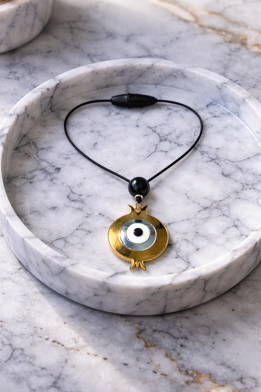Car charm with a gold pendant and black beads on a marble surface