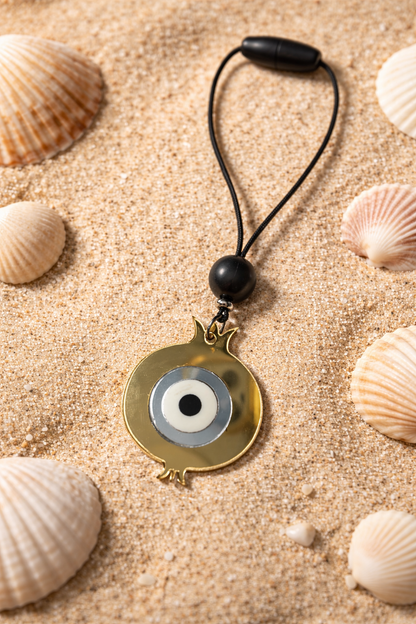 Evil eye pendant on a black cord with seashells on sand