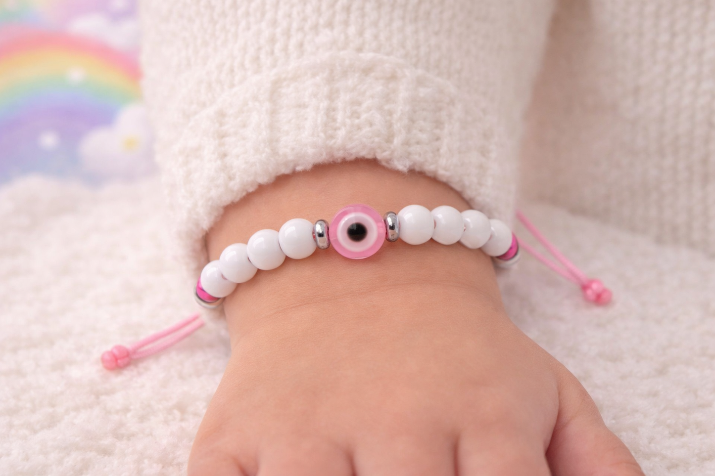 Baby's foot wearing a white beaded bracelet with pink accents on a soft surface.