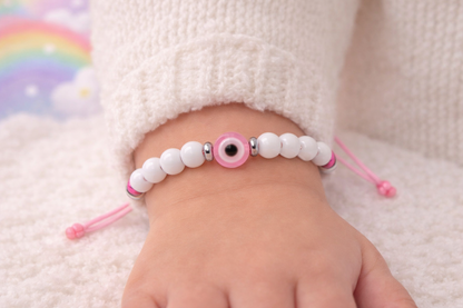 Baby's foot wearing a white beaded bracelet with pink accents on a soft surface.