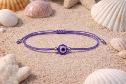 Purple bracelet with a blue evil eye bead on sand with shells