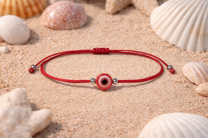 Red string bracelet with a evil eye charm on sand with seashells