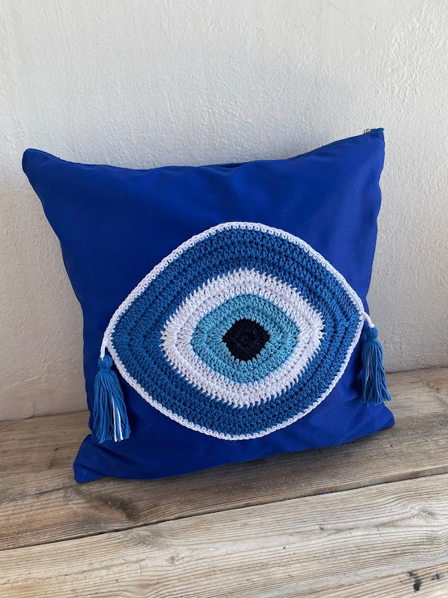 Blue pillow with a crochet eye design on a wooden surface