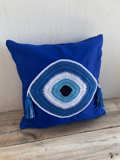Blue pillow with a crochet eye design on a wooden surface