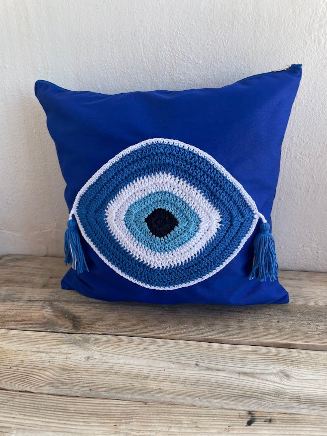 Blue pillow with a crochet eye design on a wooden surface