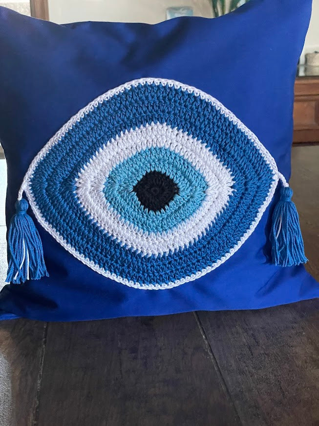 Blue pillow with a crochet eye design on a wooden surface