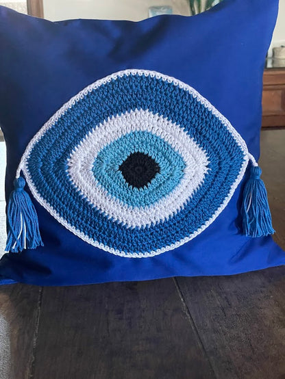 Blue pillow with a crochet eye design on a wooden surface