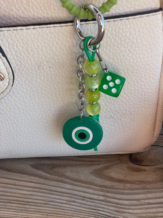 A blue silicone evil eye bag charm with a stainless steel chain and resin beads attached to a handbag.