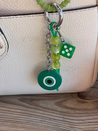 A blue silicone evil eye bag charm with a stainless steel chain and resin beads attached to a handbag.