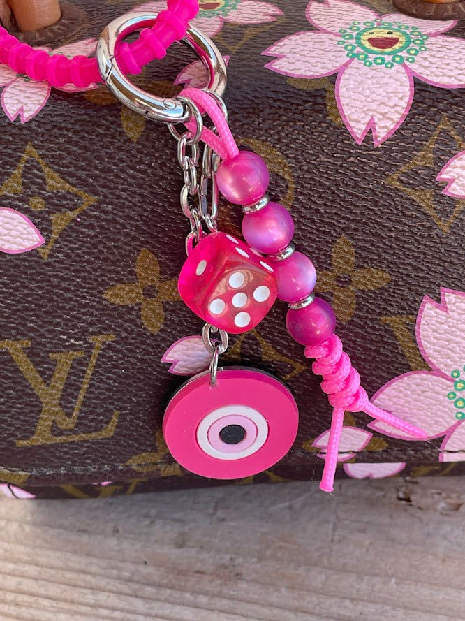 A blue silicone evil eye bag charm with a stainless steel chain and resin beads attached to a handbag.