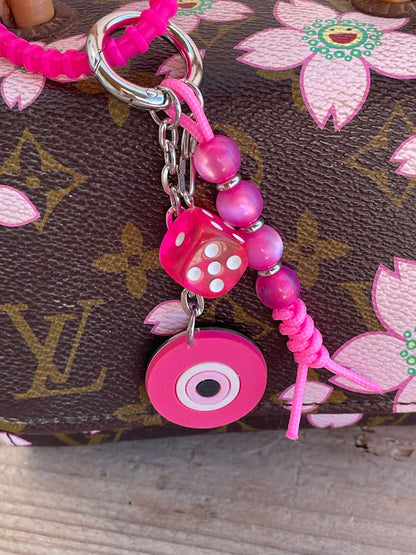 A blue silicone evil eye bag charm with a stainless steel chain and resin beads attached to a handbag.