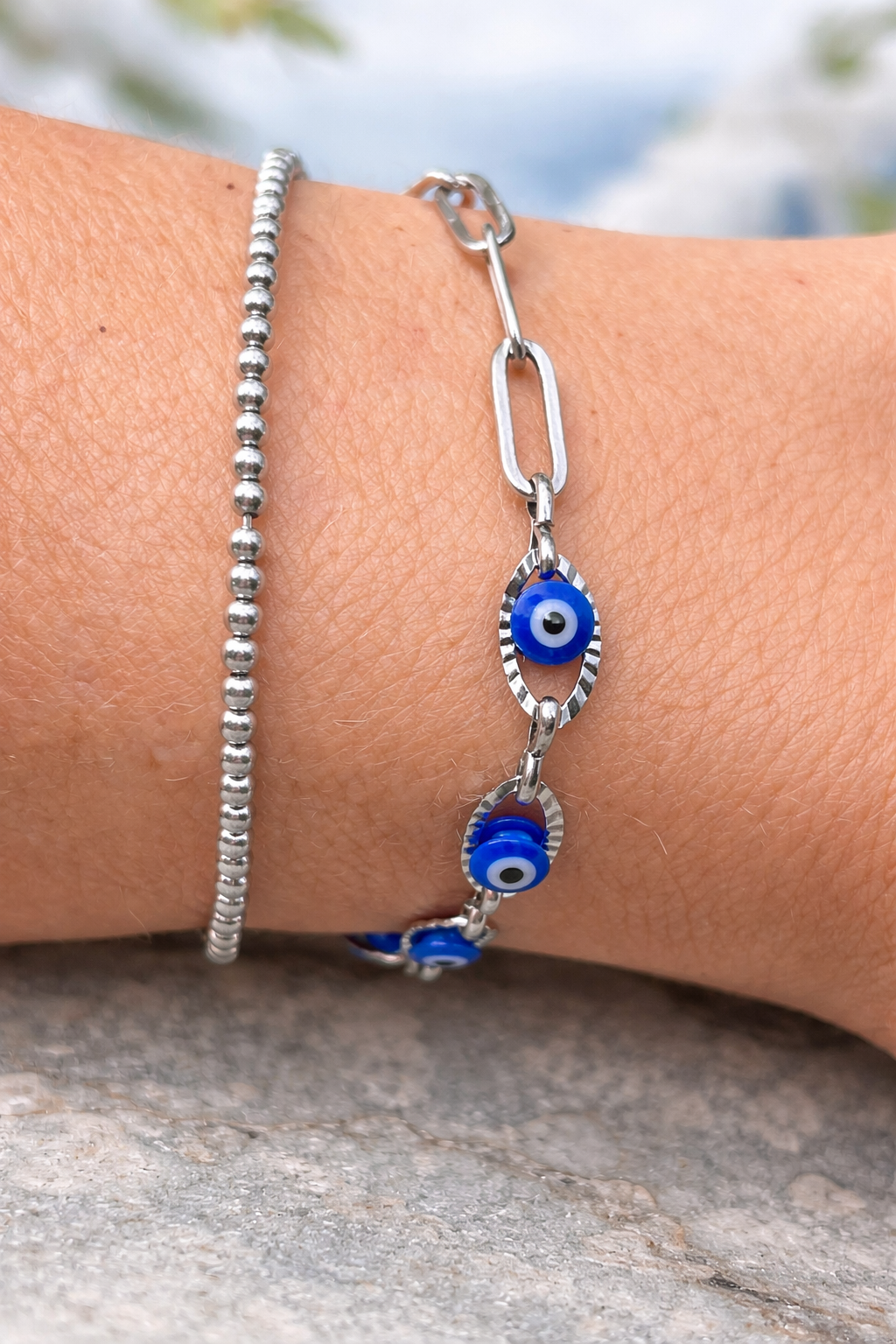 Silver bracelet with blue evil eye charm on a wrist against a blurred natural background