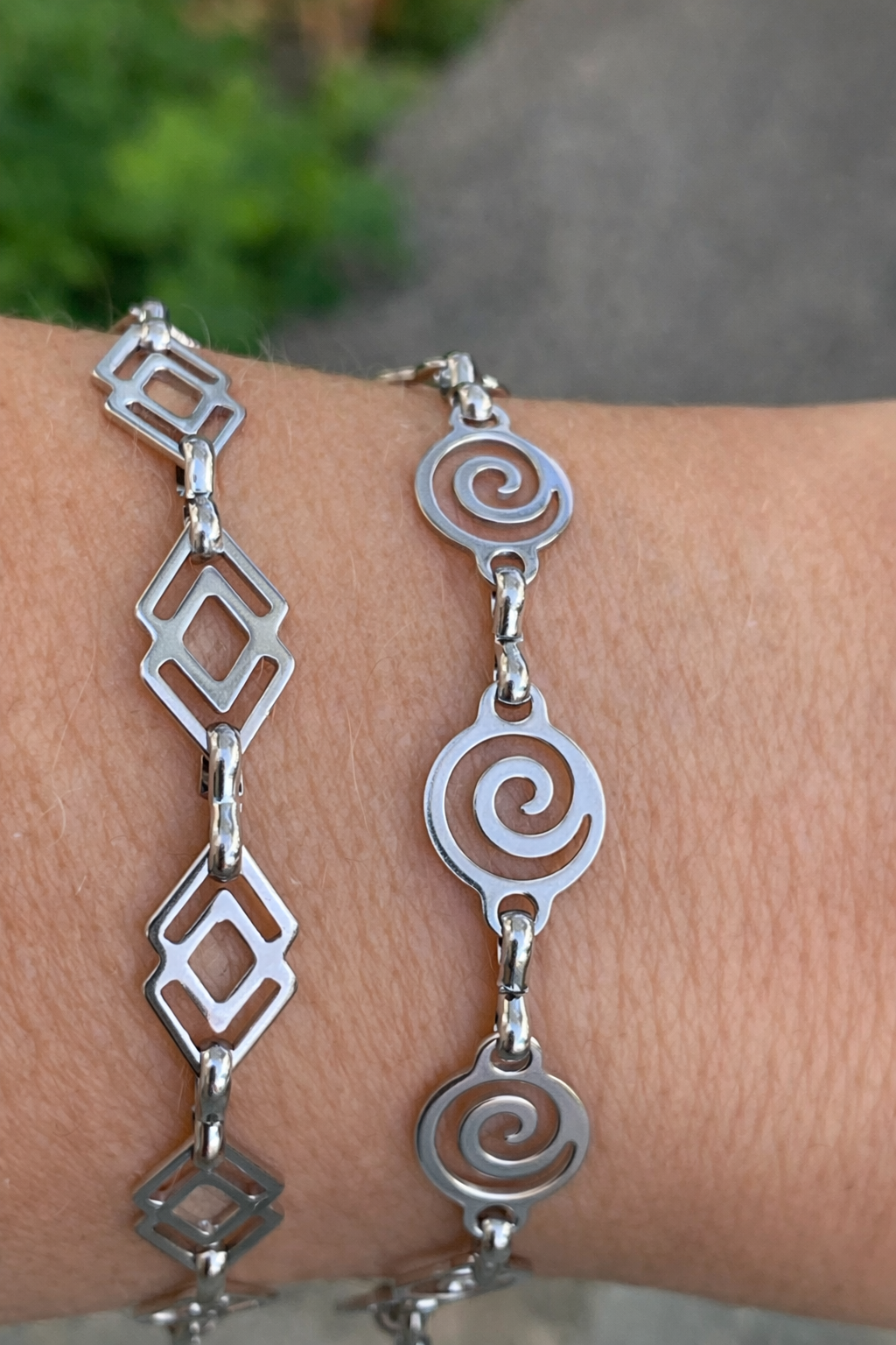 Silver bracelets with geometric and spiral designs on a wrist against a blurred natural background.