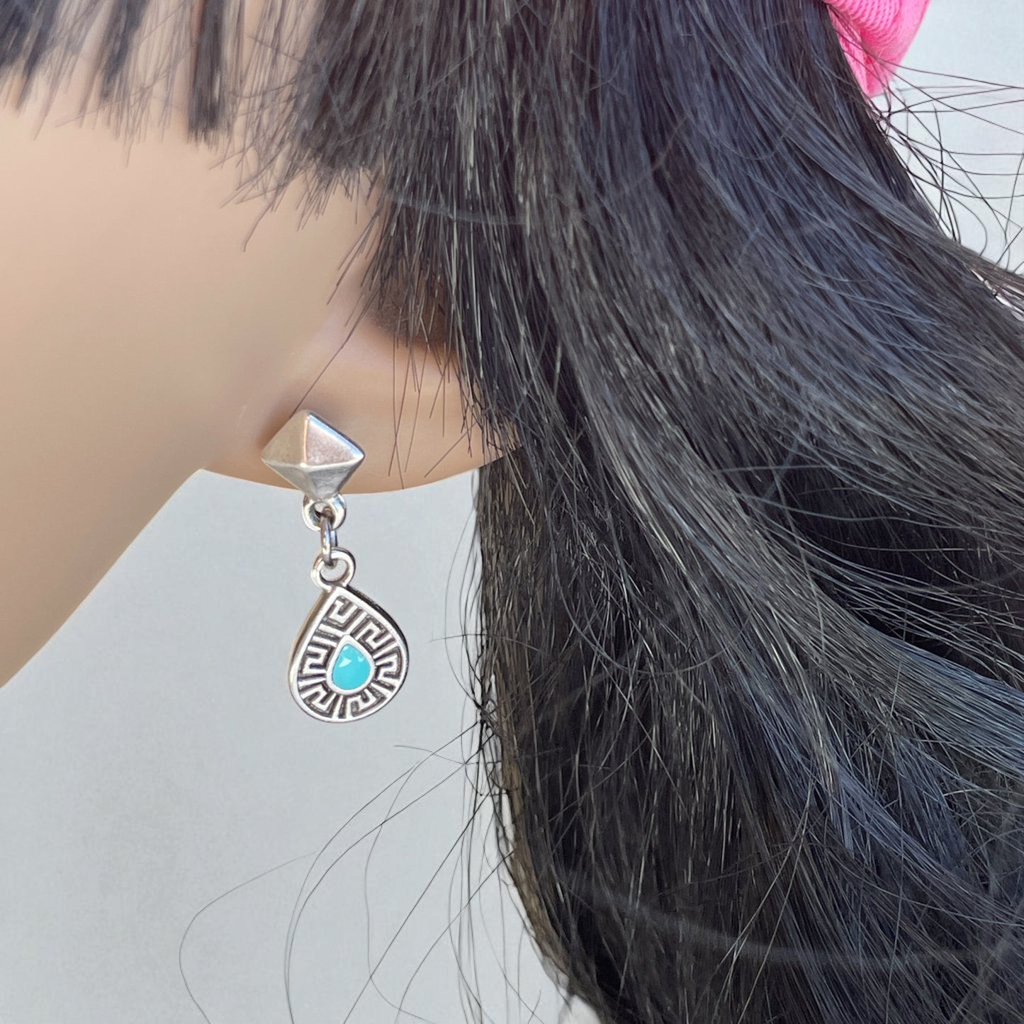 Close-up of an earring with a turquoise stone on a mannequin head.