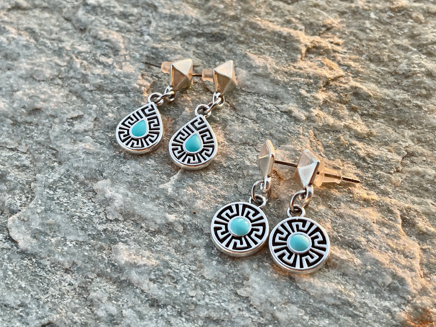 Pair of silver earrings with turquoise stones on a stone surface