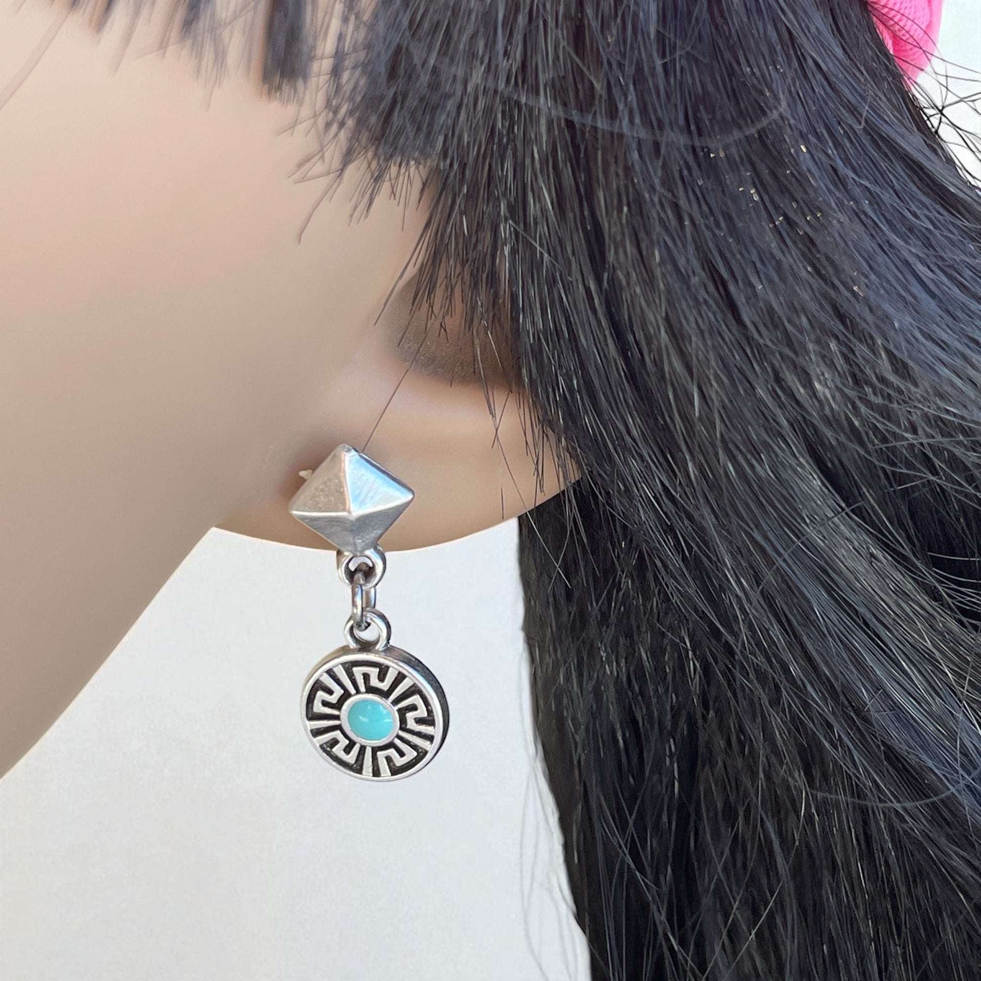 Earring with pyramid and circular design on a mannequin with black hair.