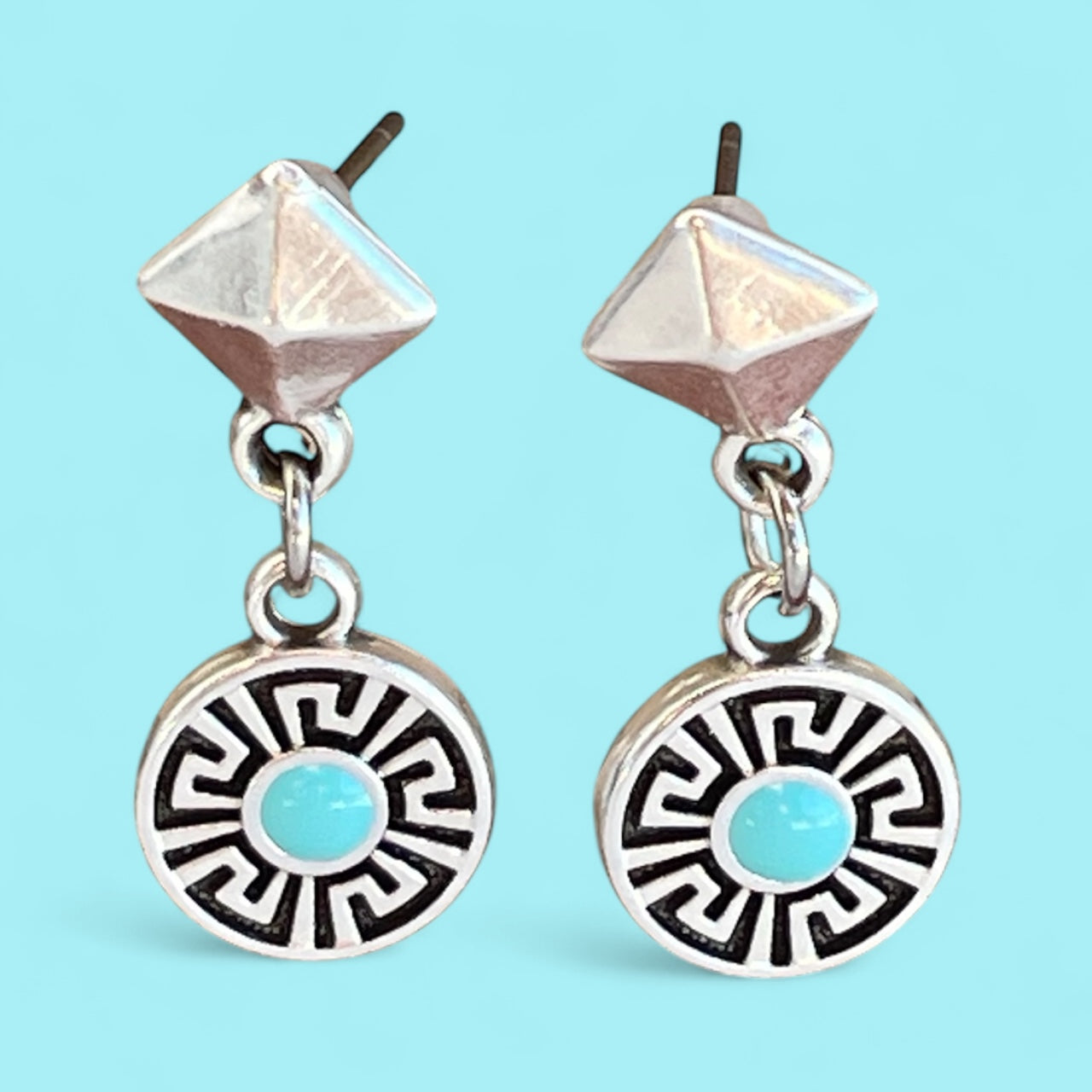 Pair of silver earrings with turquoise stones on a light blue background