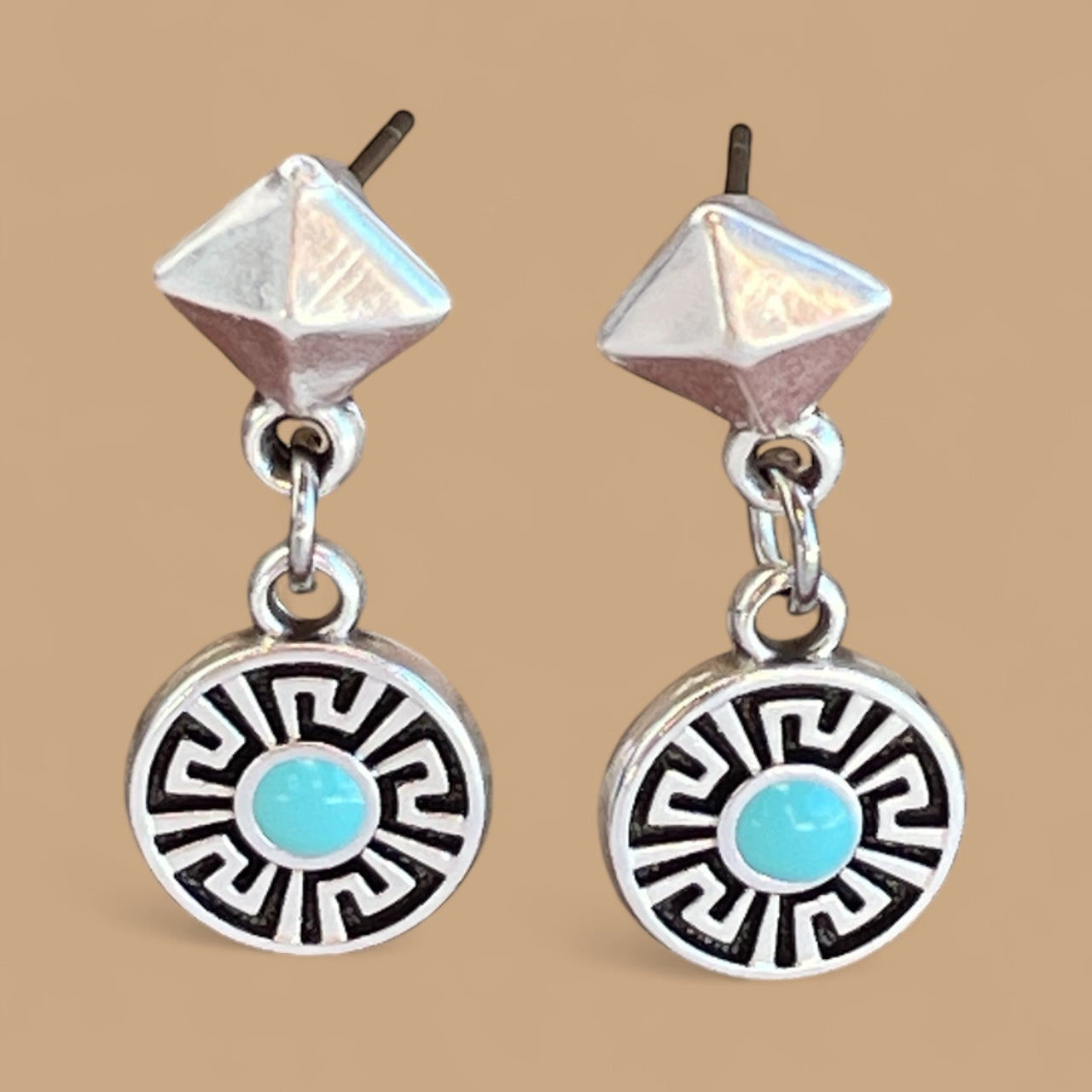 Pair of silver earrings with turquoise stones on a beige background