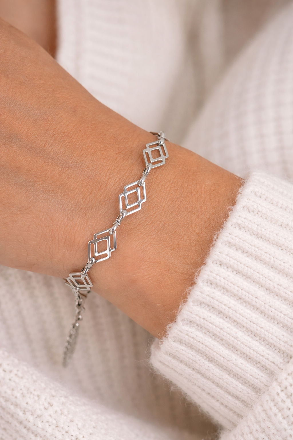 Silver geometric bracelet on a wrist with a neutral background