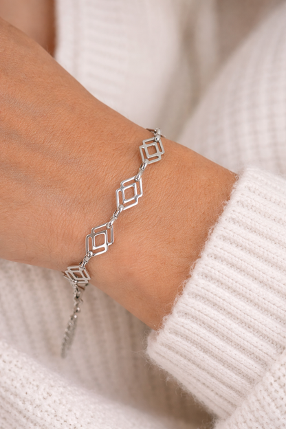 Silver geometric bracelet on a wrist with a neutral background