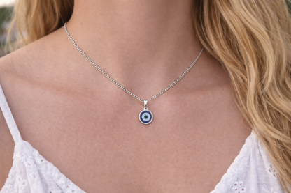 Necklace with a blue evil eye pendant worn by a person in a white top.