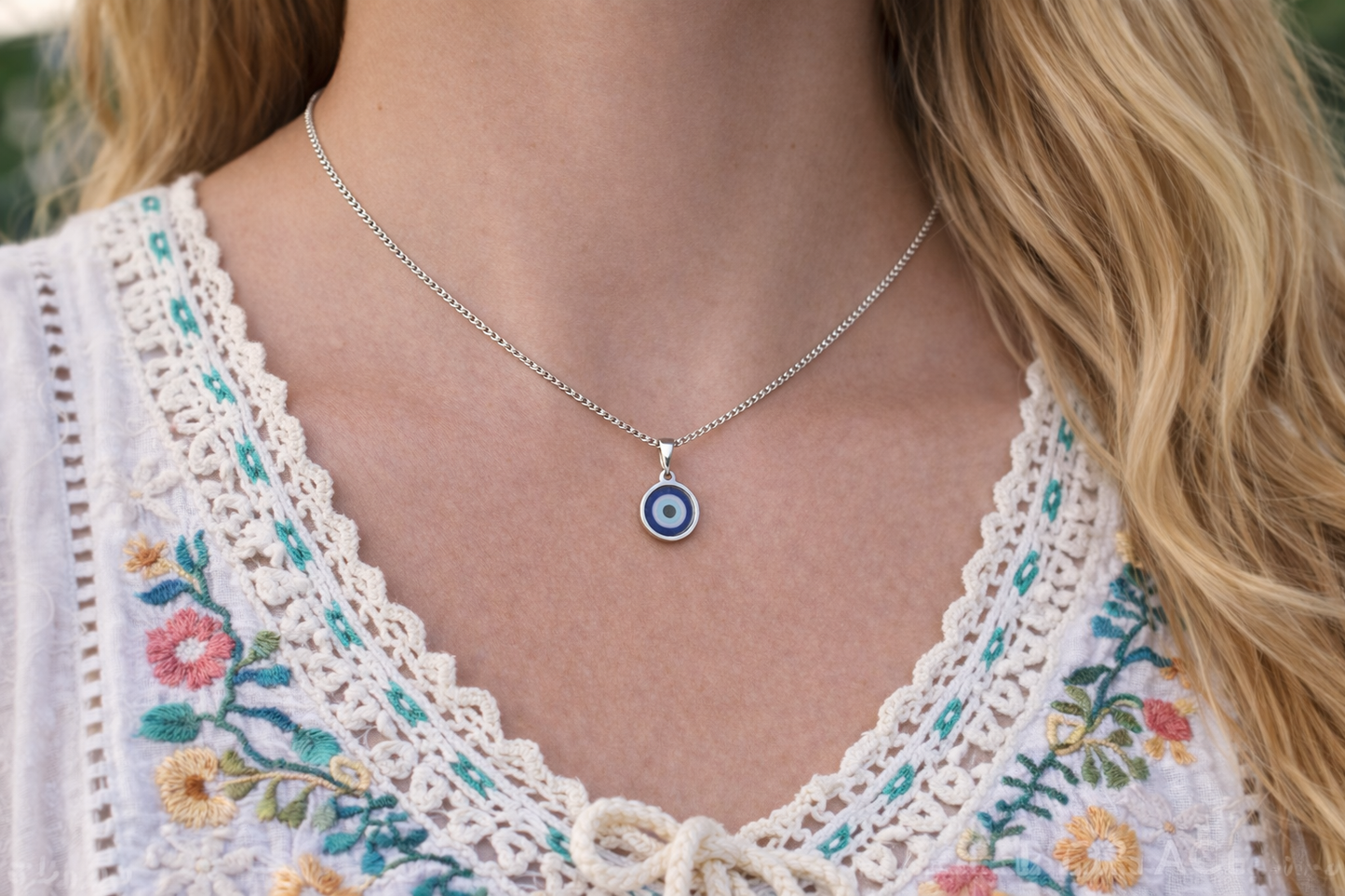 Necklace with a blue eye pendant worn by a person in a floral top.