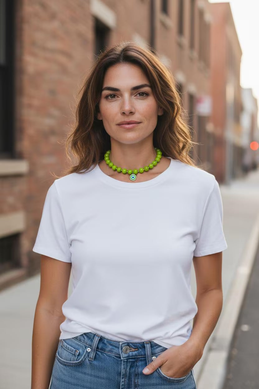 Woman wearing a white t-shirt and blue jeans with a green necklace, standing on a street.