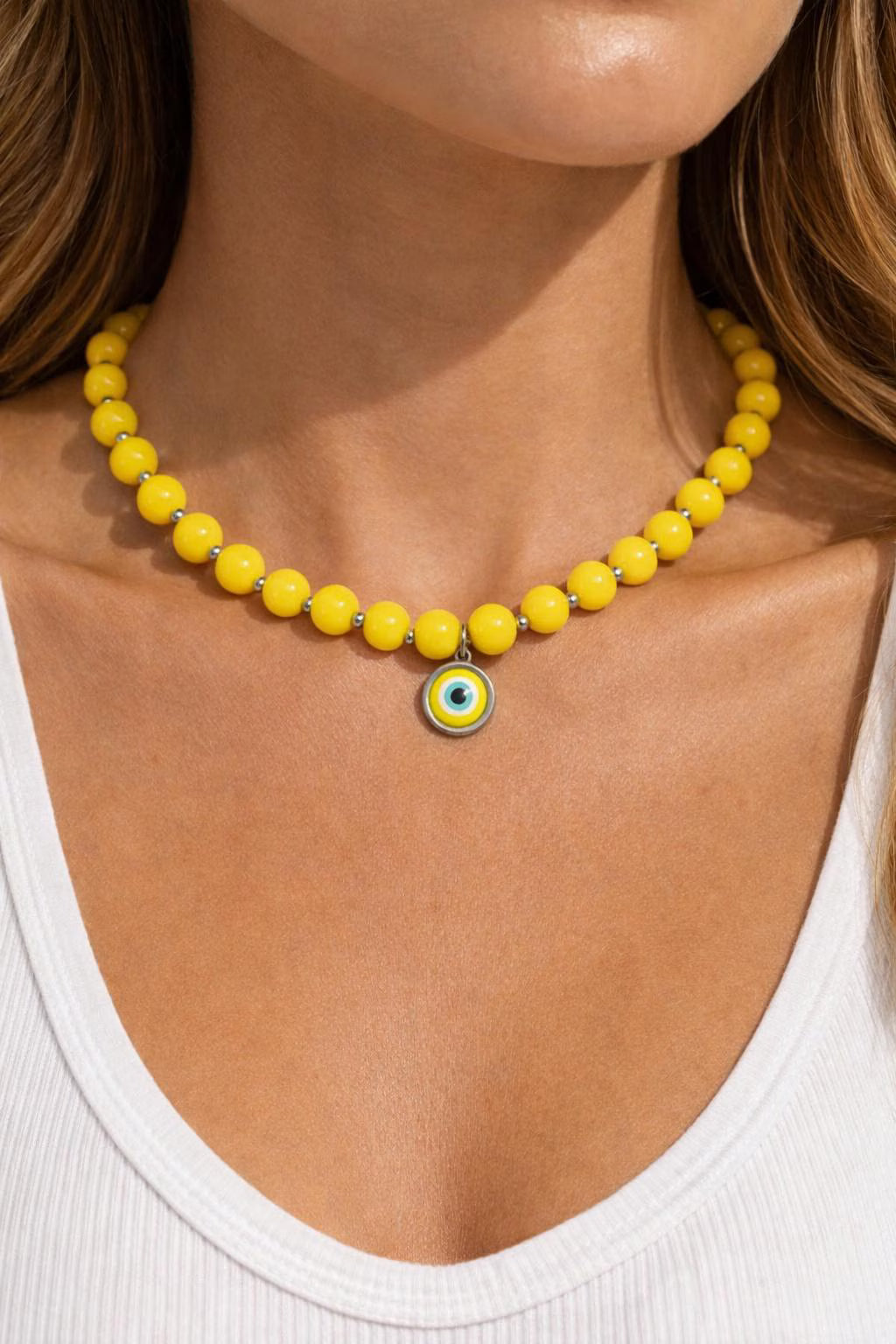 Yellow beaded necklace with a blue and yellow evil eye pendant on a person wearing a white top.