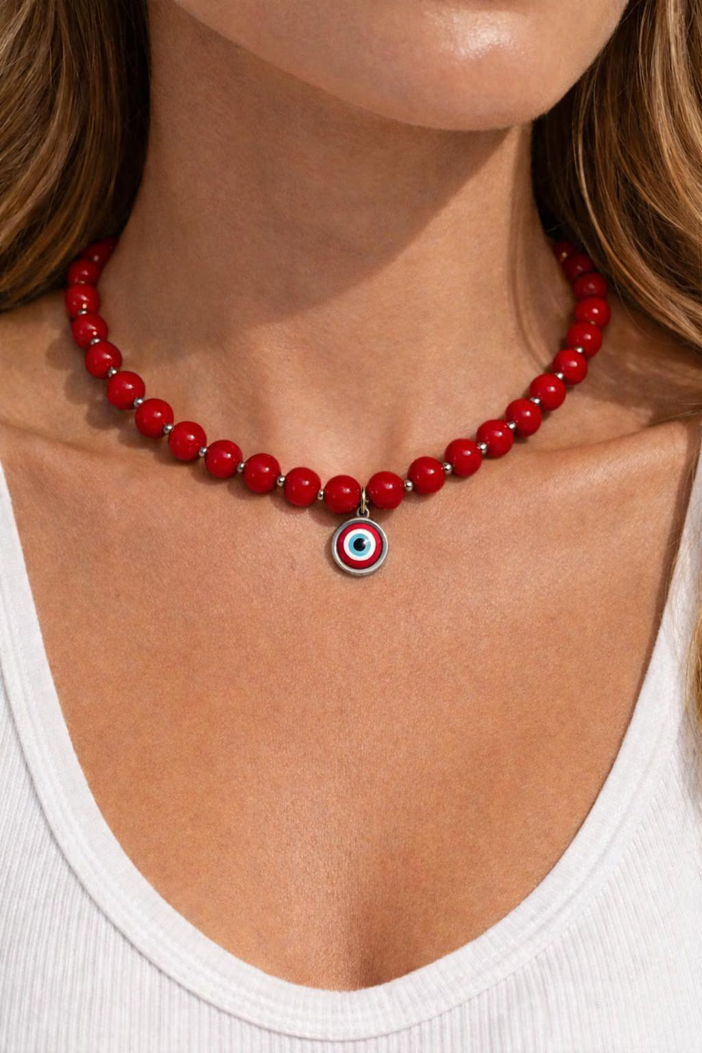 Red beaded necklace with a silver pendant on a person wearing a white top.