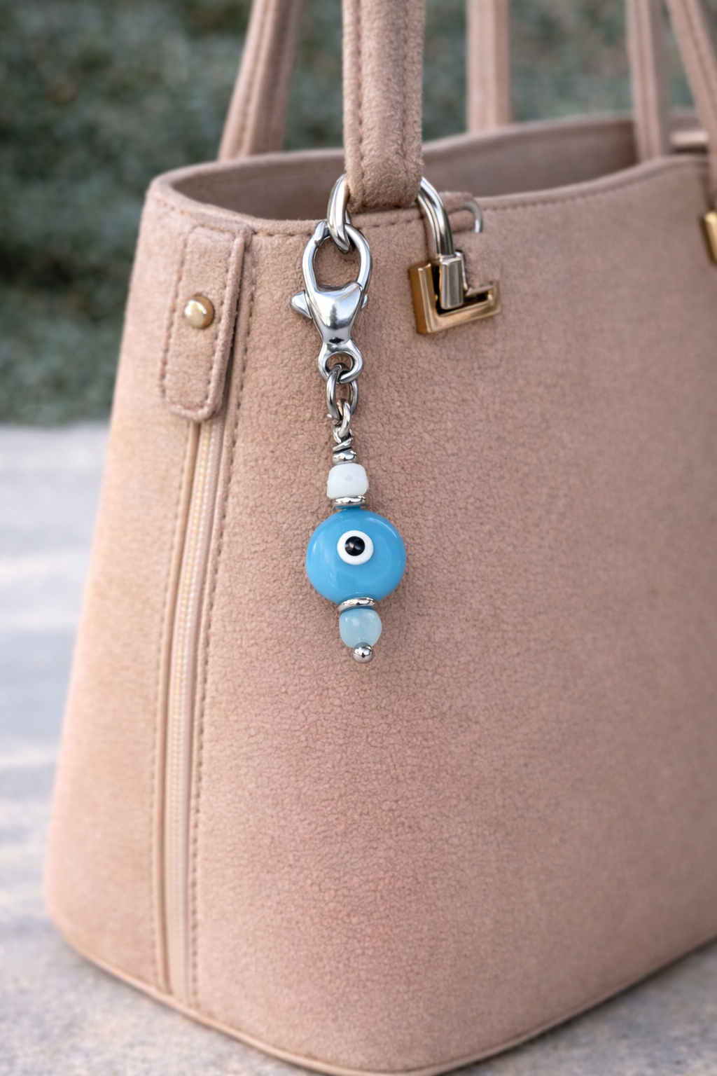 Beaded keychain with a blue evil eye charm attached to a beige handbag.