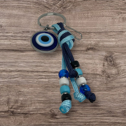 Keychain with blue and black braided cord and evil eye charm on a wooden surface