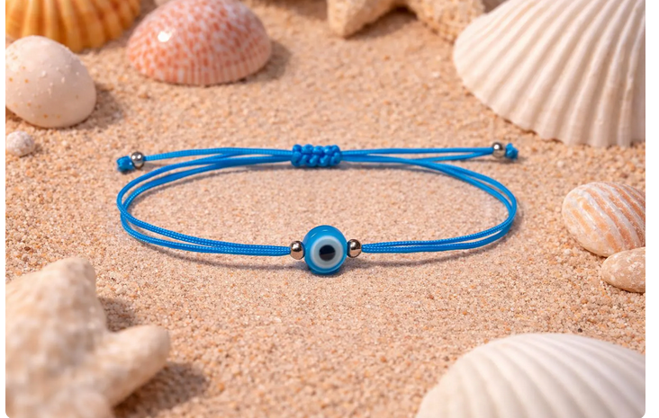 Blue bracelet with a evil eye charm on sand with seashells