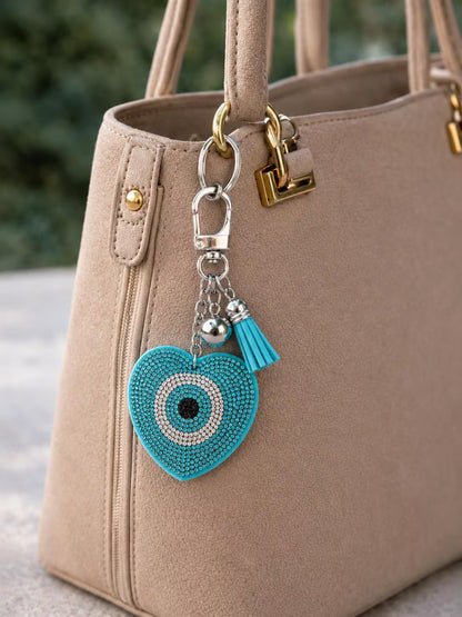 Beige handbag with a turquoise heart-shaped keychain featuring a tassel.