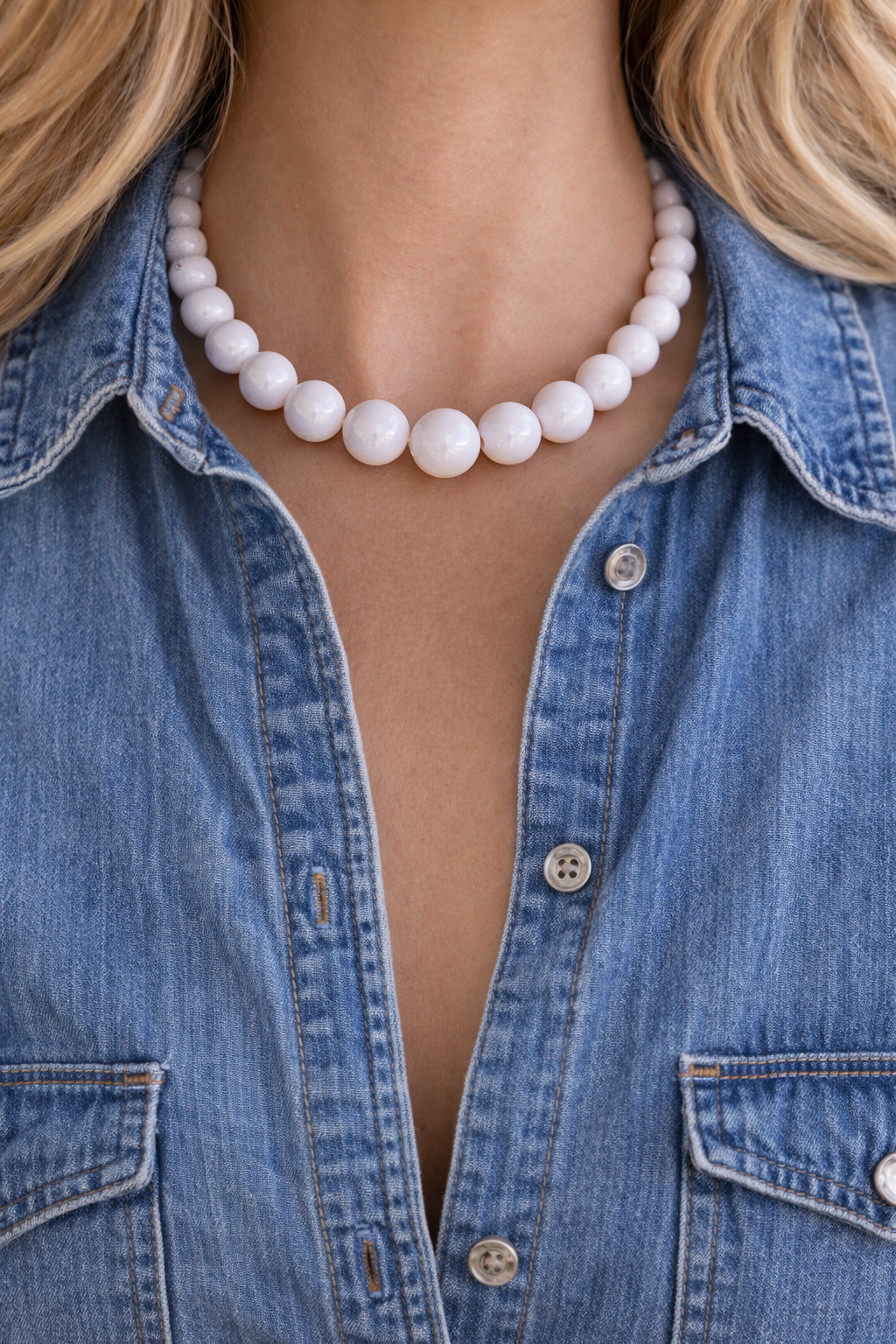 Person wearing a blue denim shirt with a pearl necklace