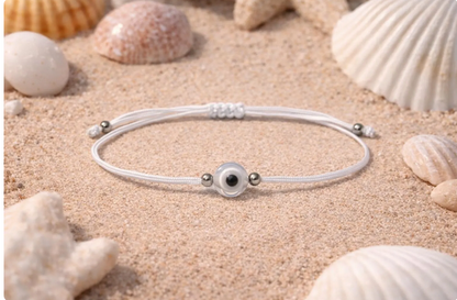 White bracelet with a black bead on sand with seashells