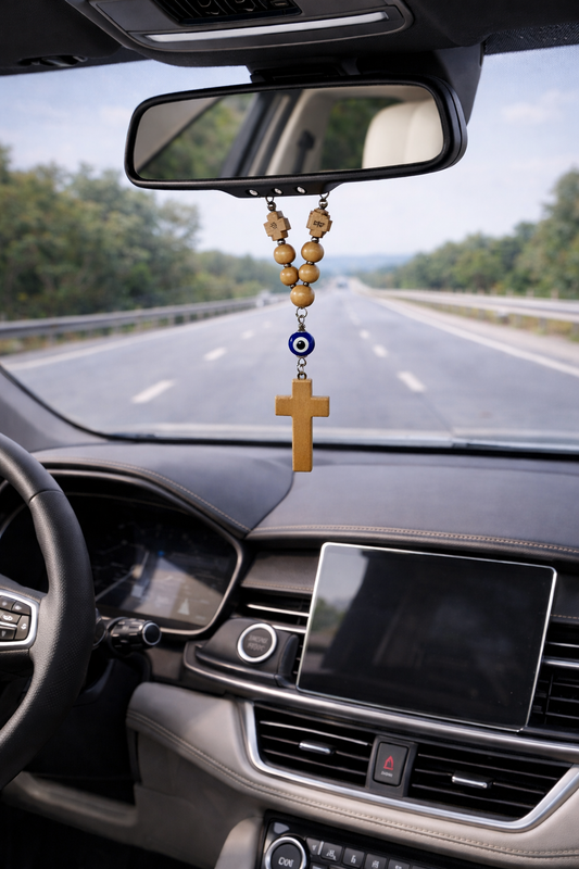 Car interior with a rosary hanging from the rearview mirror on a road.