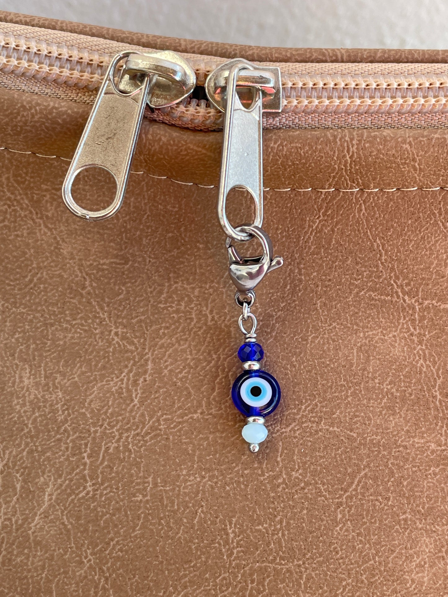 Close-up of a zipper pull with an evil eye charm on a brown leather surface