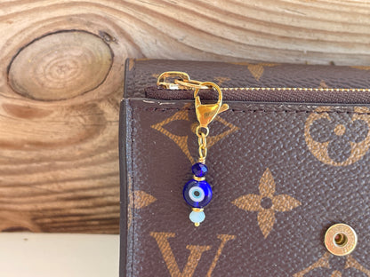 Close-up of a brown leather wallet with a gold clasp and blue evil eye charm on a wooden surface.