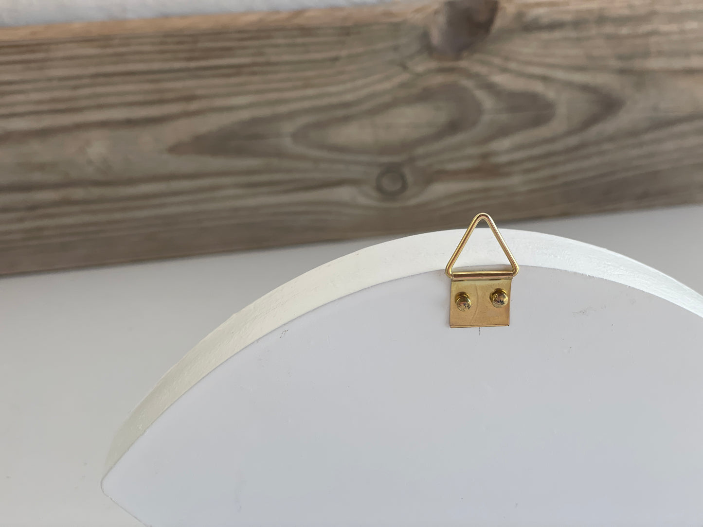 Gold triangle-shaped hook on a white circular frame against a wooden background