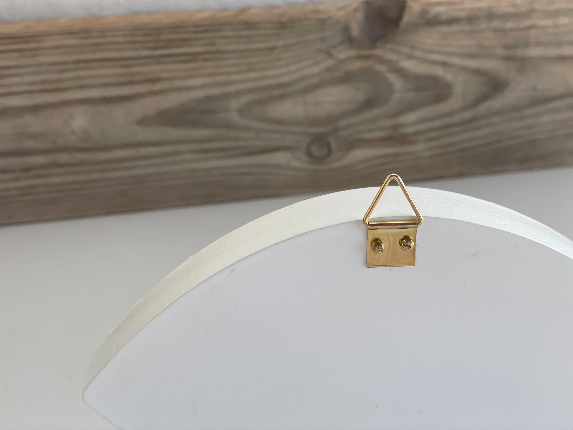 Gold triangle-shaped hook on a white circular frame against a wooden background
