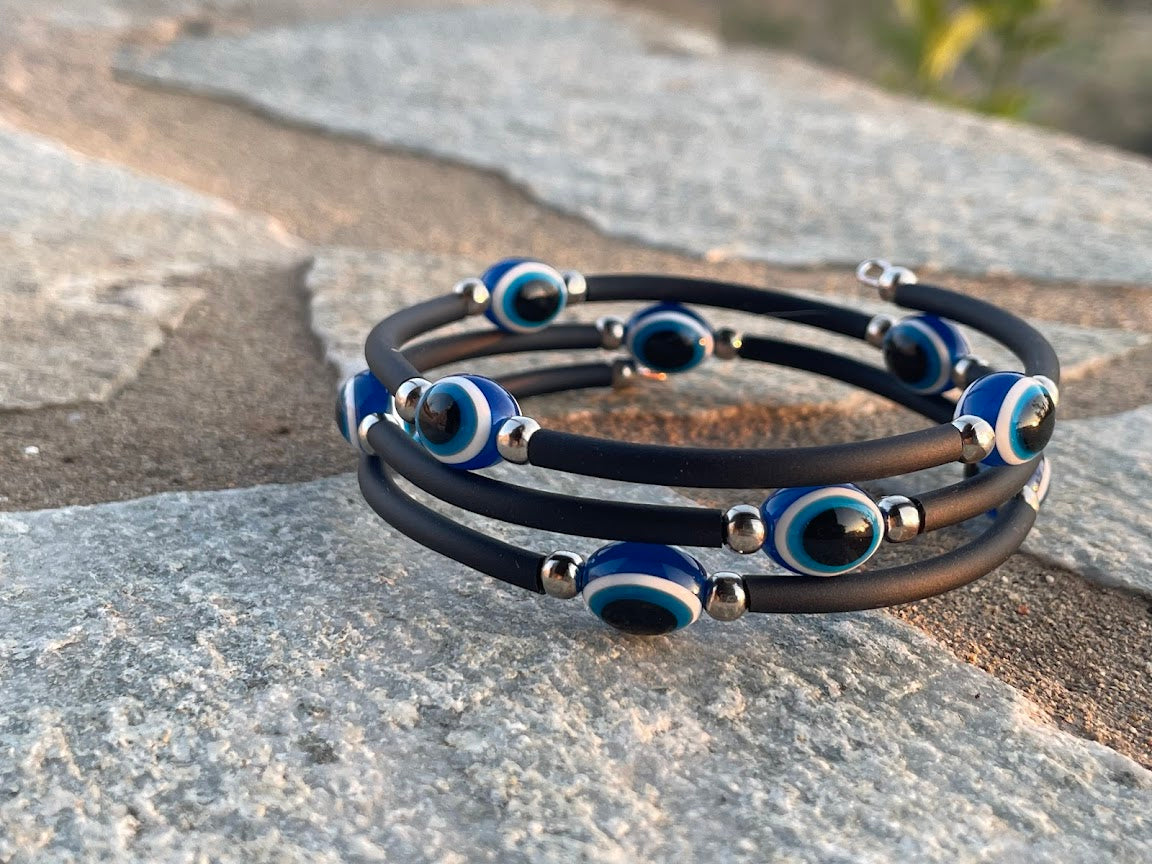 Stack of black leather bracelets with blue evil eye charms on a stone surface