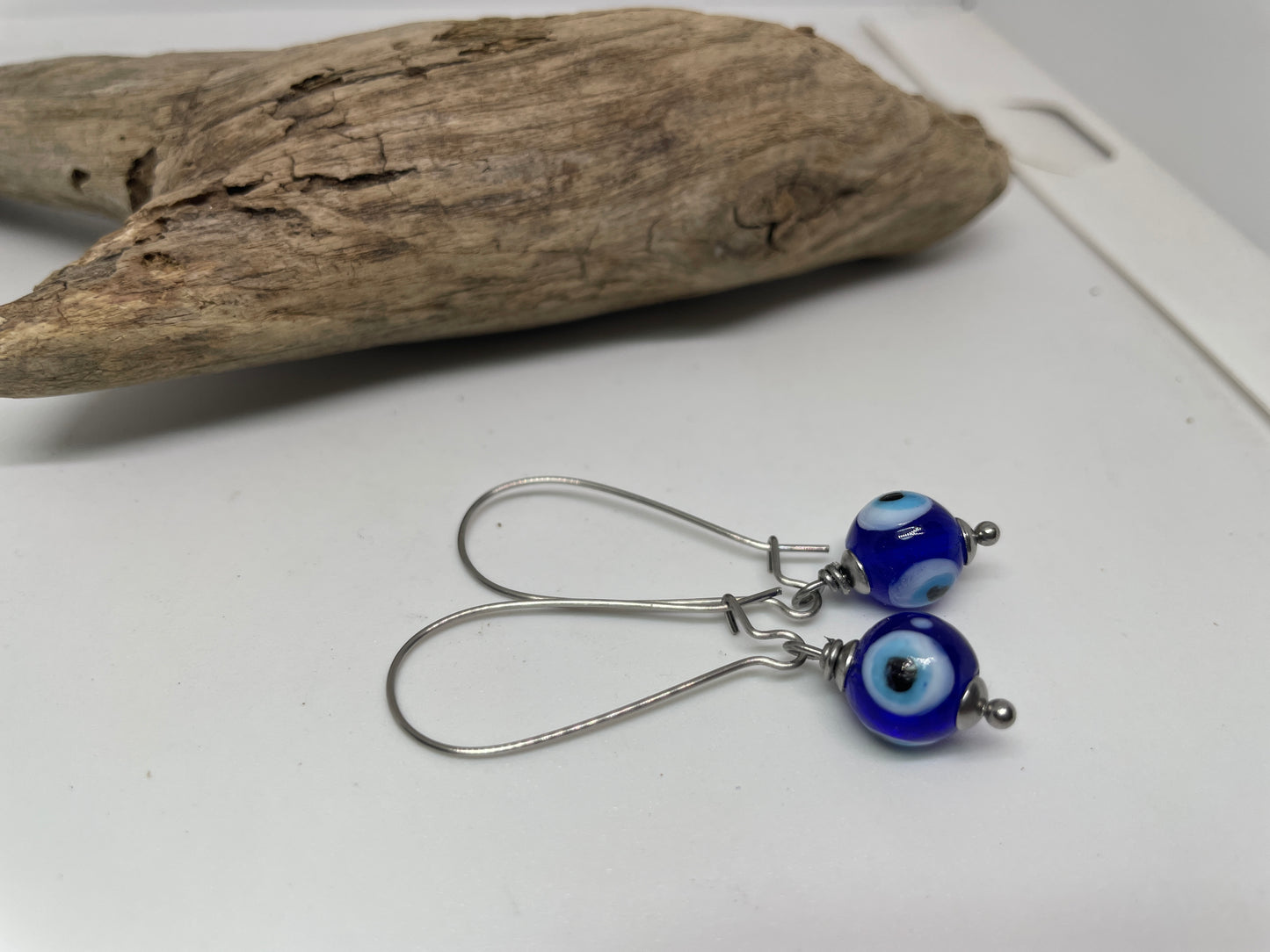 Pair of blue and silver earrings on a white surface with driftwood.