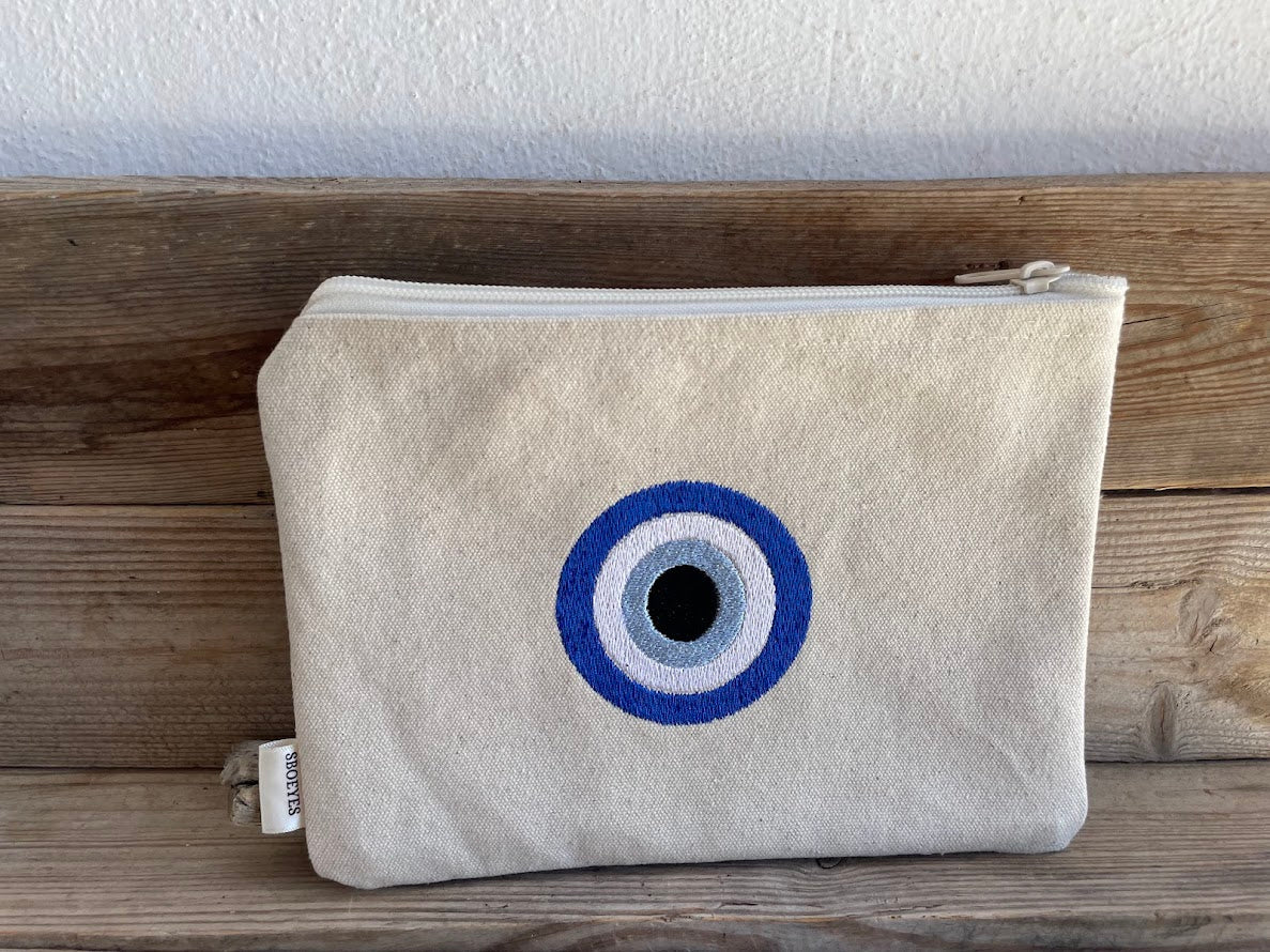 Beige pouch with a blue and white eye design on a wooden surface