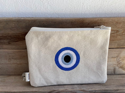 Beige pouch with a blue and white eye design on a wooden surface