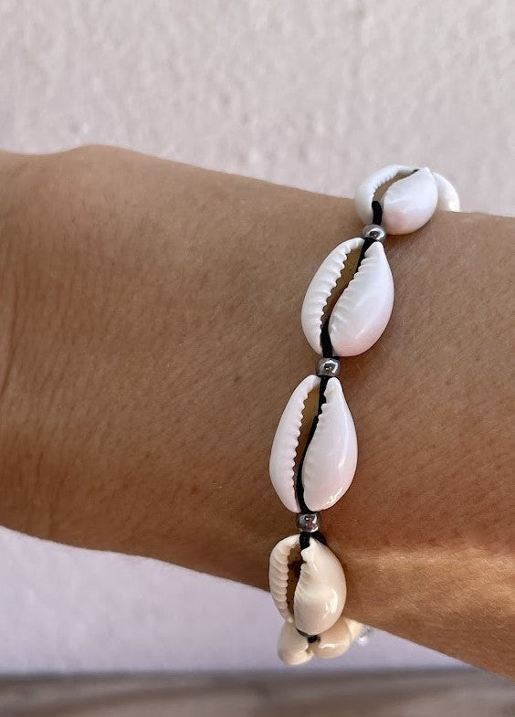 Bracelet with cowrie shell beads on a wrist against a neutral background