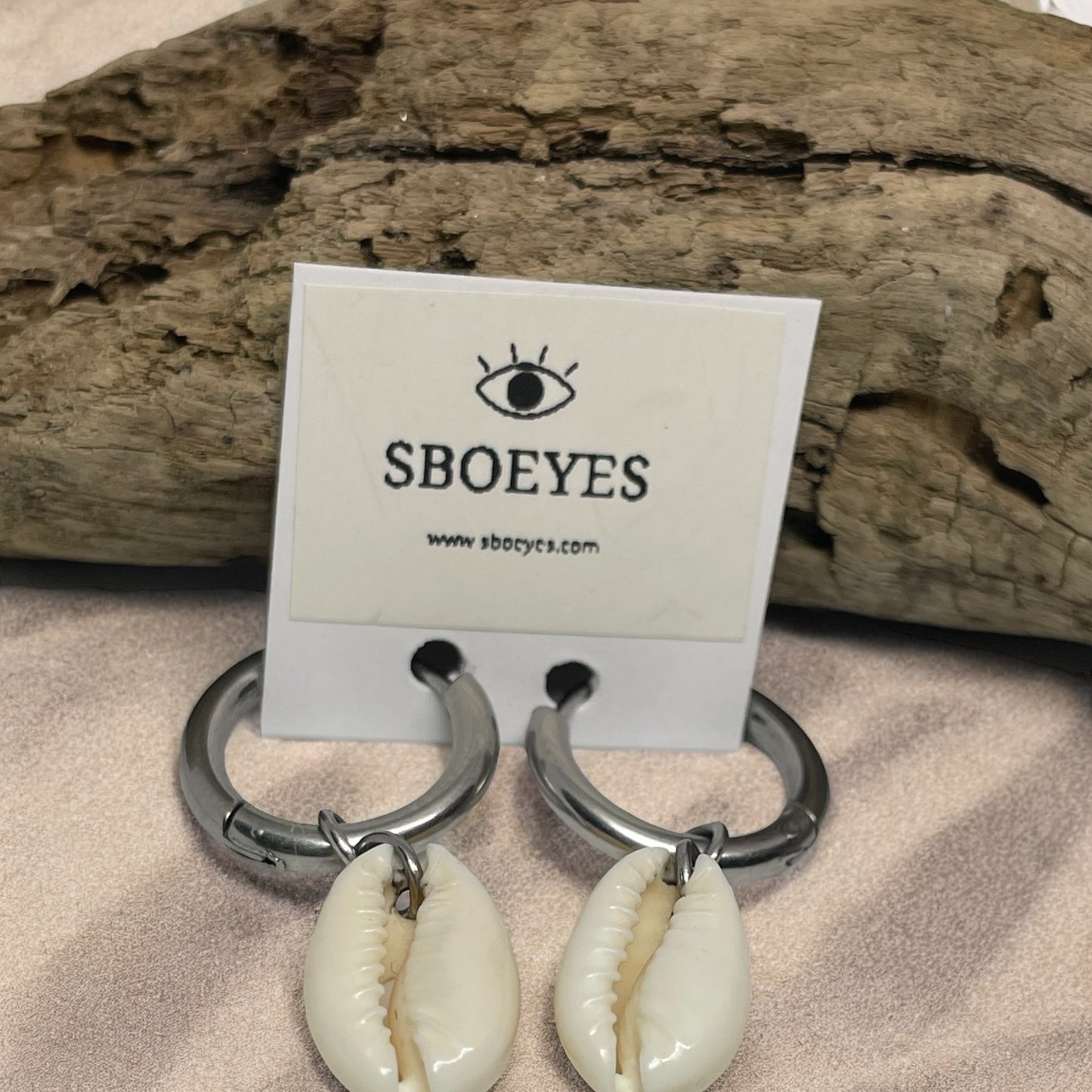 Shell earrings with a 'SBOEYES' card on a wooden background