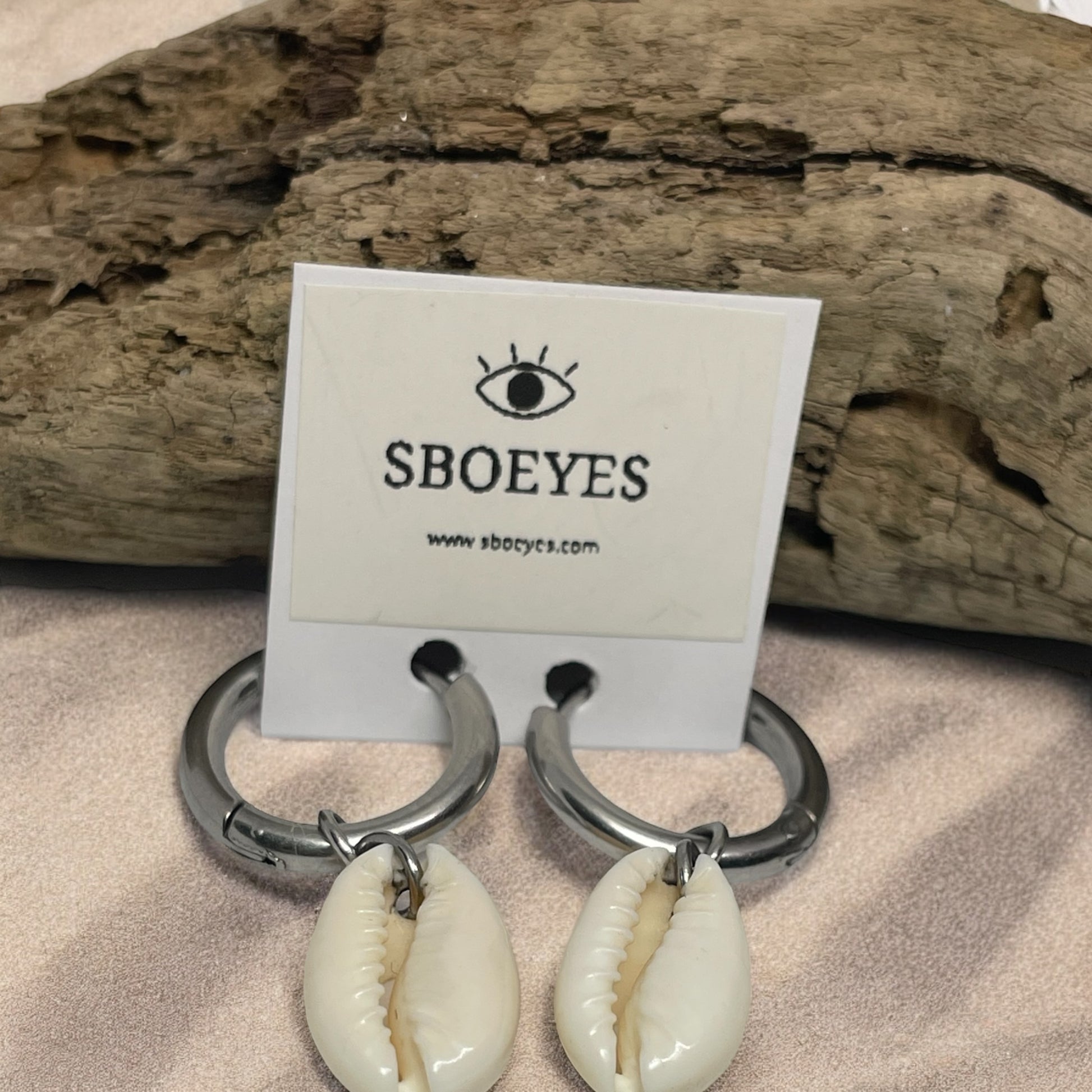 Shell earrings with a 'SBOEYES' card on a wooden background