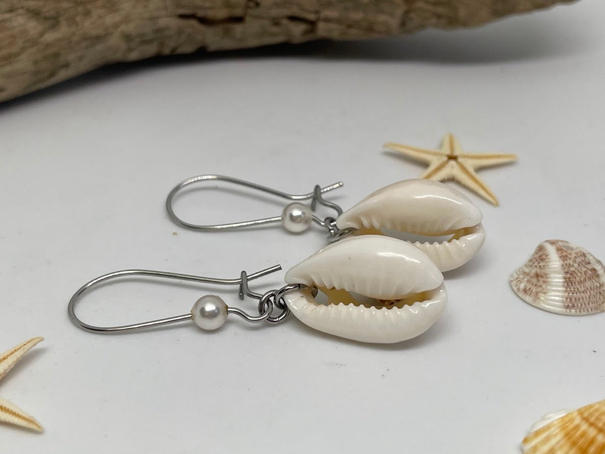 Shell earrings with silver hooks on a white surface with starfish and shells.